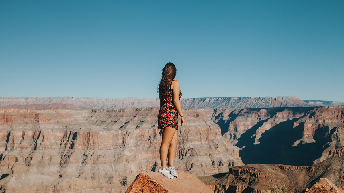 dziewczyna w letnim stroju stoi na krawędzi Grand Canyon i patrzy w stronę kanionu